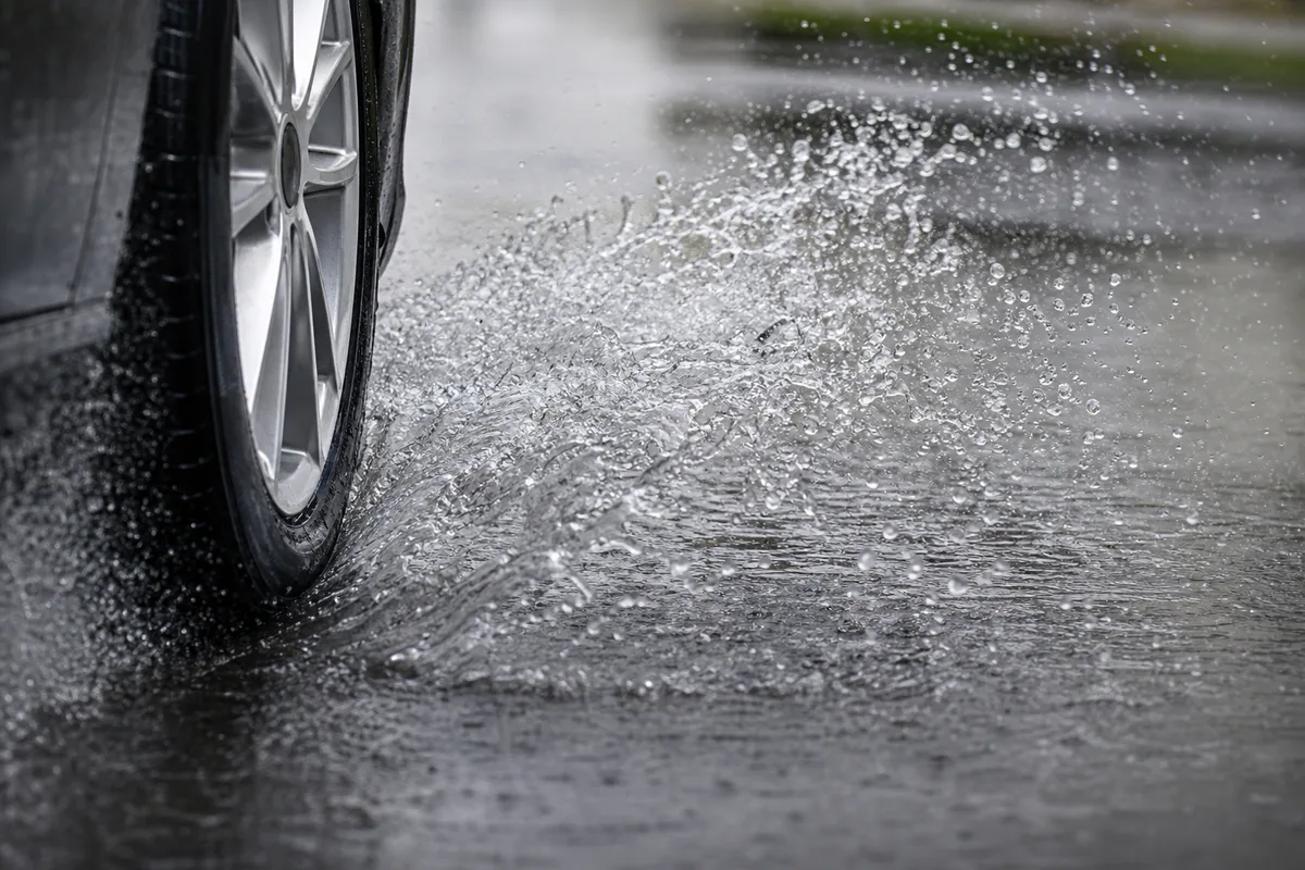 Pneu de voiture projetant une gerbe d’eau sur une chaussée détrempée